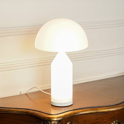 Minimal table lamp with glowing white dome shade on wooden surface creating warm ambient lighting for cozy interior setting.