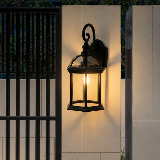 Black metal outdoor wall light lifestyle image with clear glass panels casting a warm glow on a concrete gate pillar.