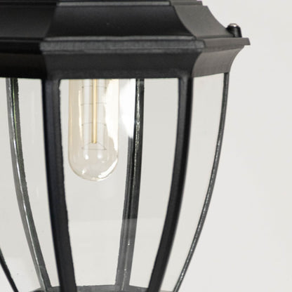 Closeup of outdoor wall lantern showing black metal frame clear glass panels and filament bulb highlighting classic exterior lighting.