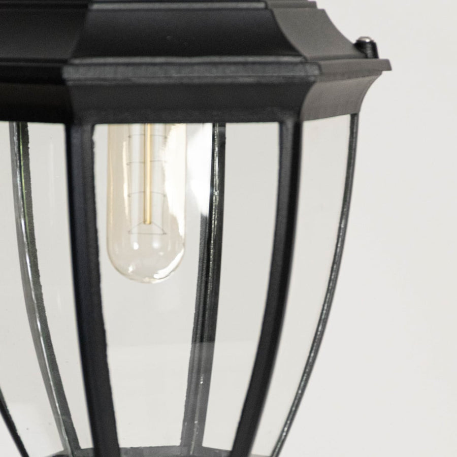 Closeup of outdoor wall lantern showing black metal frame clear glass panels and filament bulb highlighting classic exterior lighting.