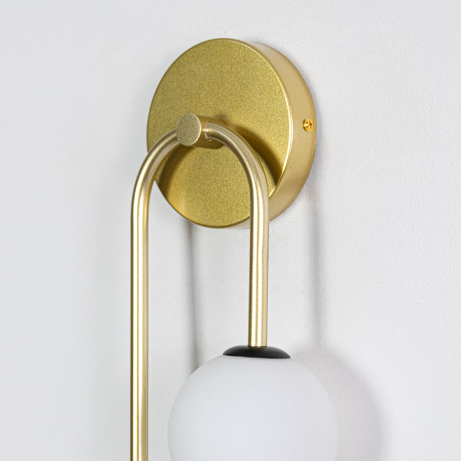 A close detailed view of the gold wall light showing the smooth metal finish and the connection between the frosted globe and circular rings in a refined modern design.