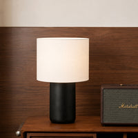 Black ceramic table lamp with white fabric shade creating warm ambient lighting on bedside table in modern interiors.