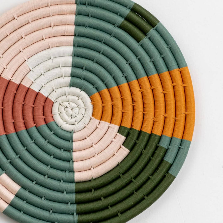 Closeup of handcrafted multicolor seagrass wall basket with green peach white and mustard woven pattern for home décor.