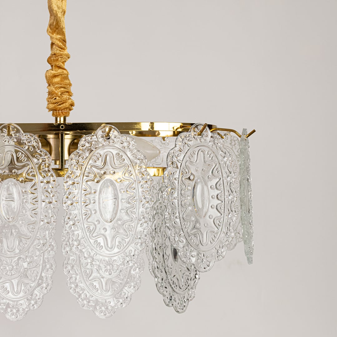 Closeup of gold metal chandelier showing ornate carved glass detailing and shimmering accents ideal for luxurious vintage interior lighting.