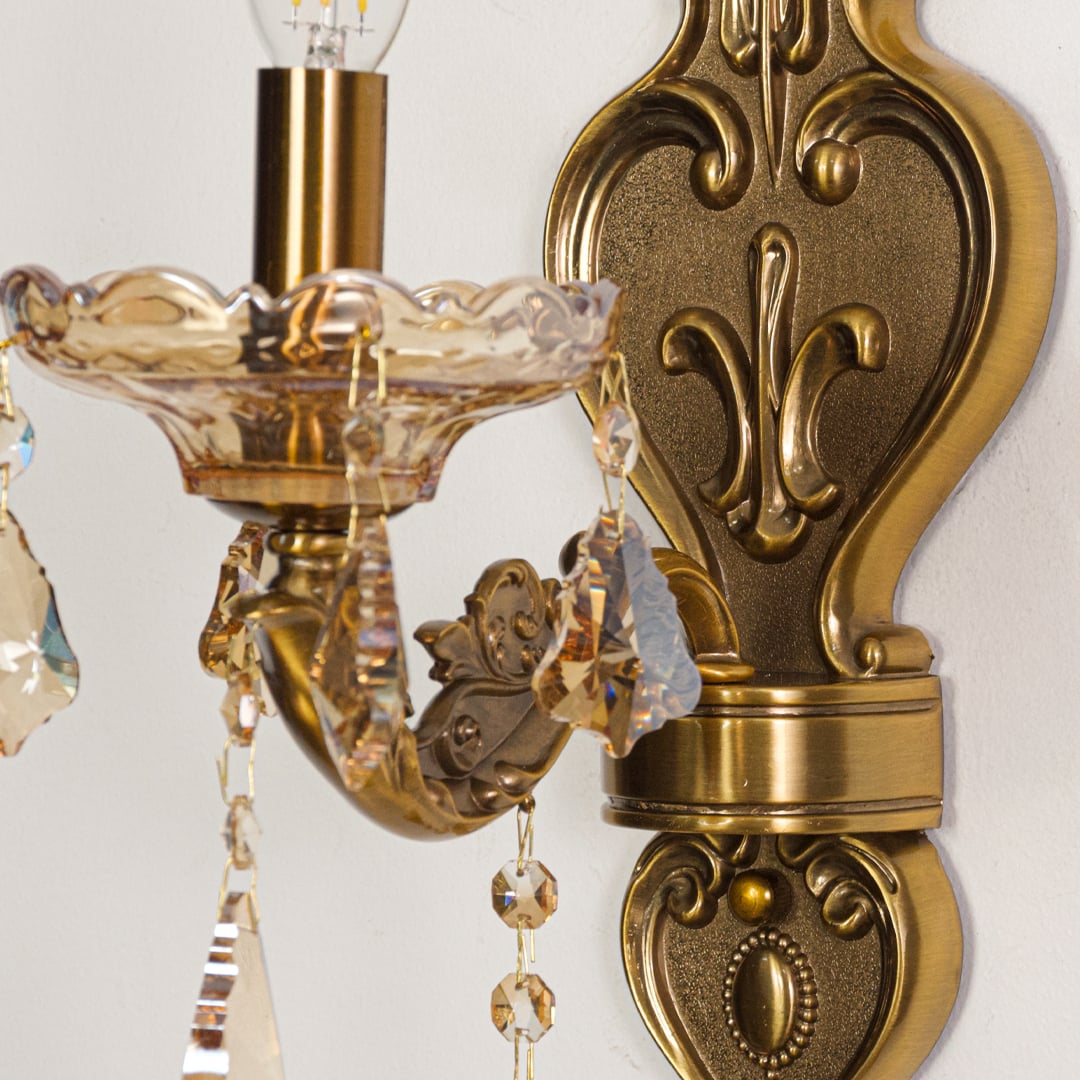 Closeup of gold wall light showing ornate metal detailing and amber crystal droplets for premium interior lighting style.