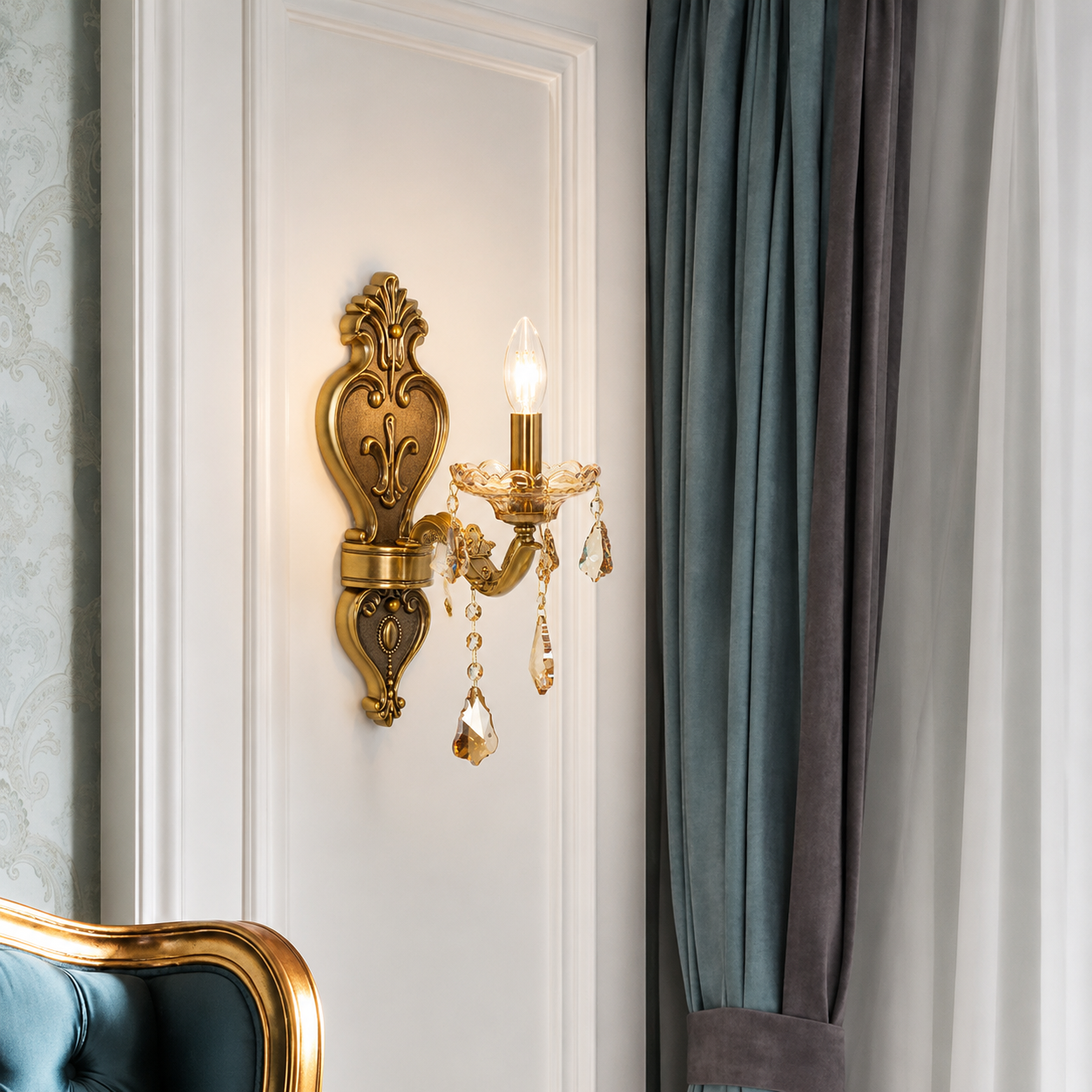 An ornate gold wall sconce with crystal droplets is mounted on a white paneled wall next to blue and gray curtains.