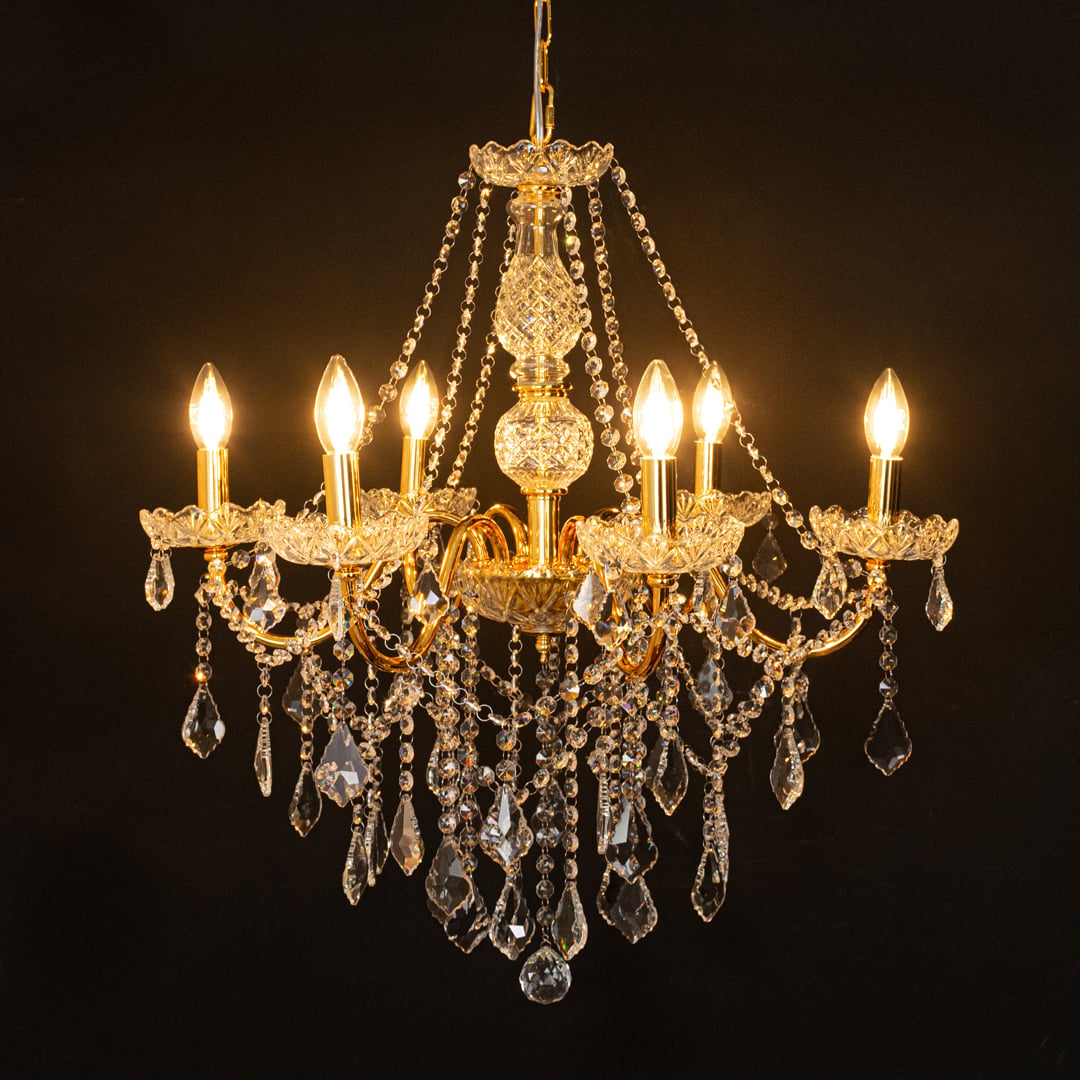 Gold metal crystal chandelier glowing warmly on black background creating a dramatic luxury ceiling feature.