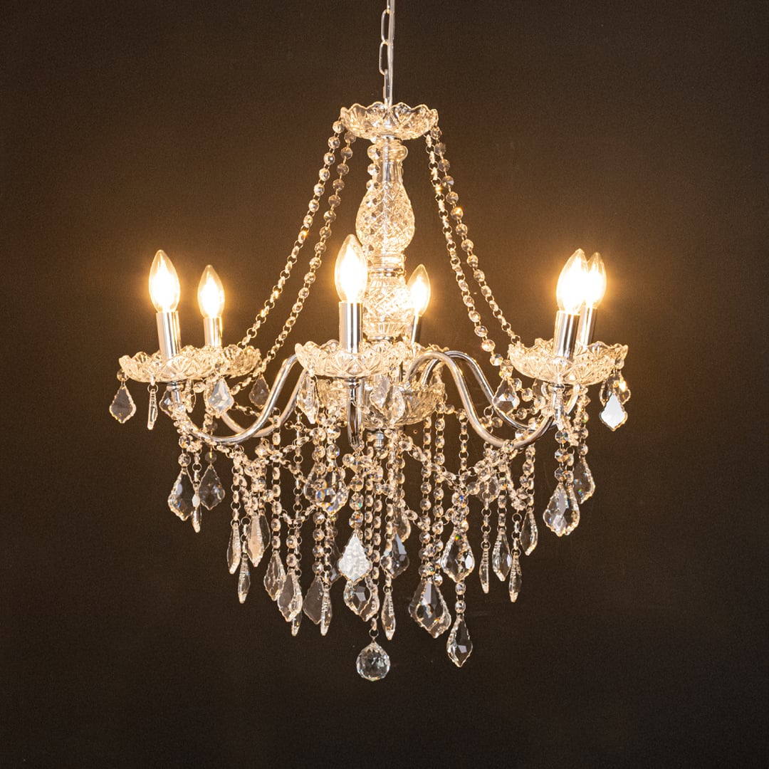 Silver metal crystal chandelier glowing warmly on black background creating a dramatic luxury ceiling feature.