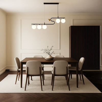 A sculptural black and gold chandelier shining softly above a neutral dining table arrangement adding refined warm LED lighting and sophisticated décor.