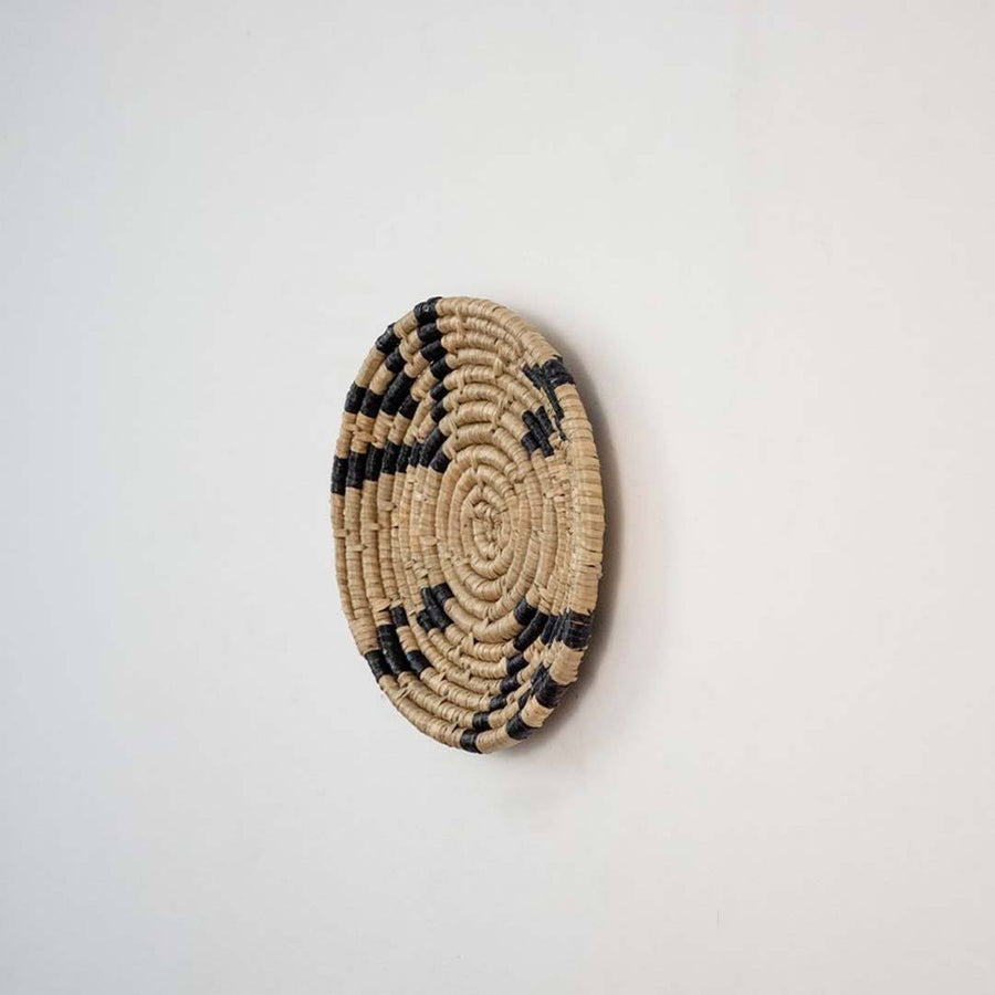 Handwoven seagrass round wall basket decor in natural beige and black with raised spiral woven profile on white background.
