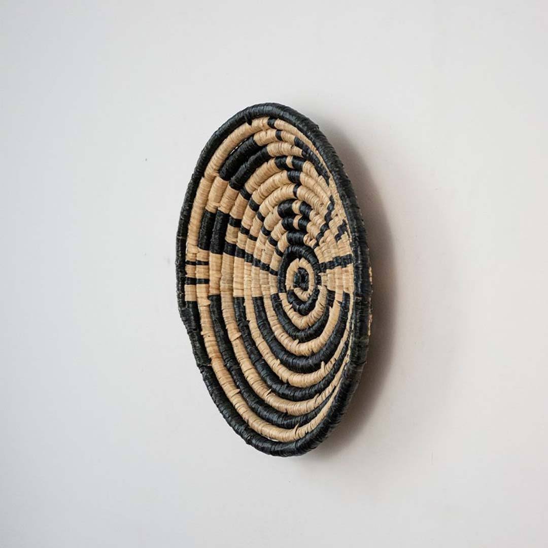 Handwoven seagrass round wall basket decor in natural beige and black with raised spiral woven profile on white background.