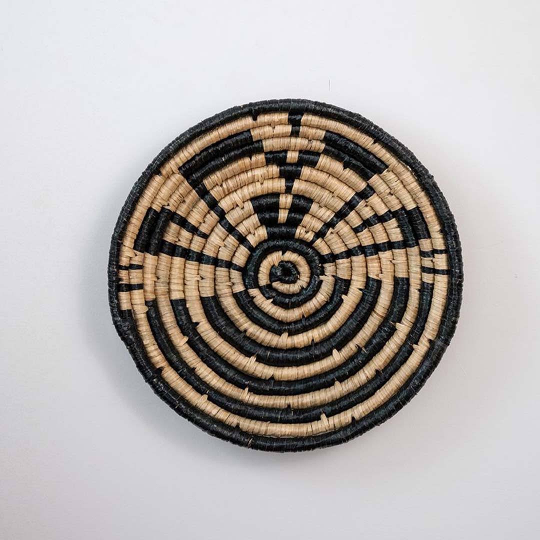 Handwoven seagrass round wall basket decor in natural beige and black with geometric spiral woven pattern on white background.