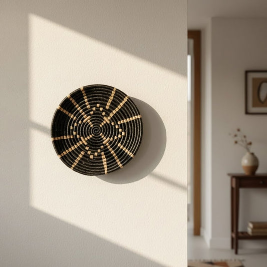 Lifestyle image showing a handcrafted round woven wall basket in black and natural tones mounted on a sunlit neutral wall adding warmth texture and artisanal character to a modern home interior.