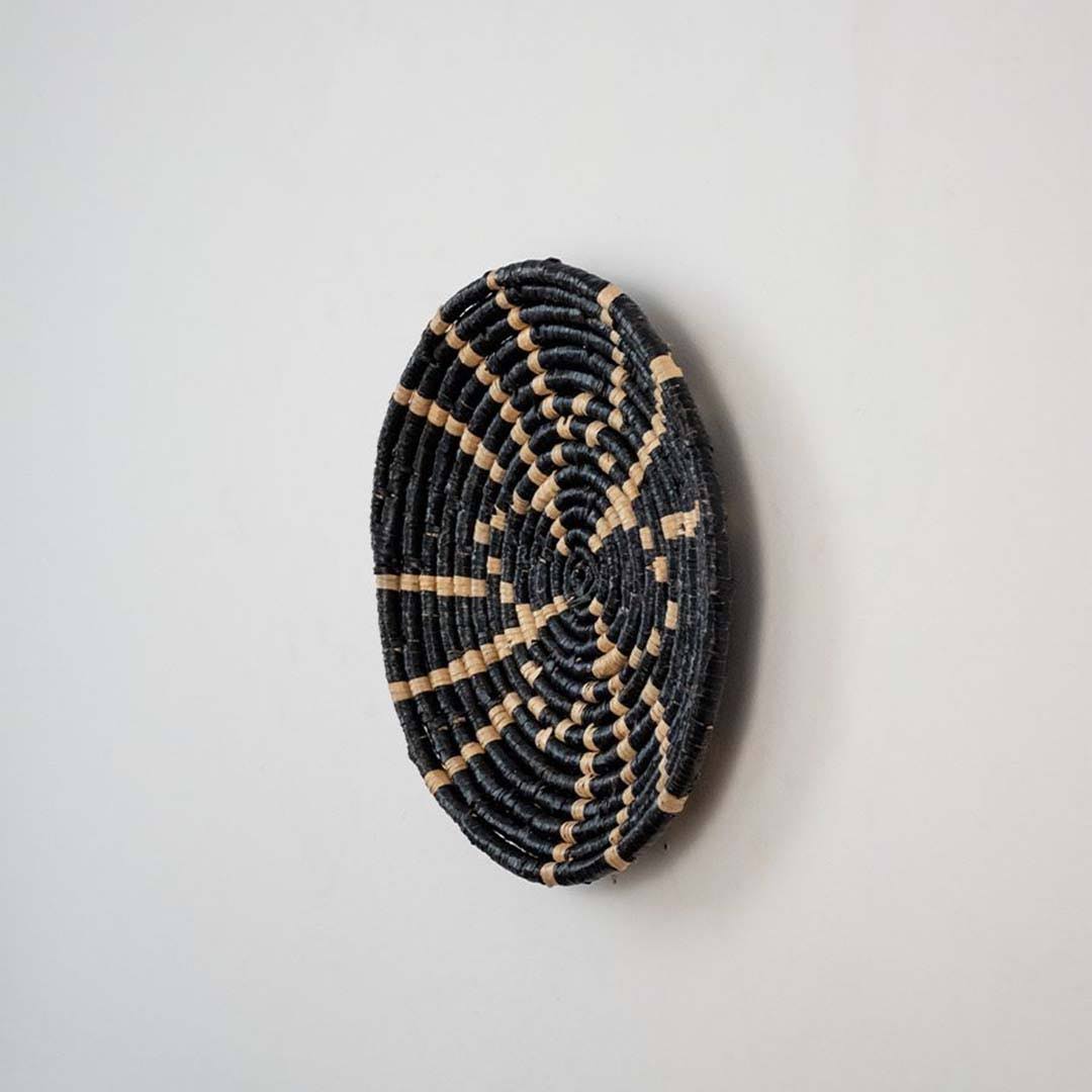 Handwoven seagrass round wall basket decor in natural beige and black with raised sunburst woven profile on white background.