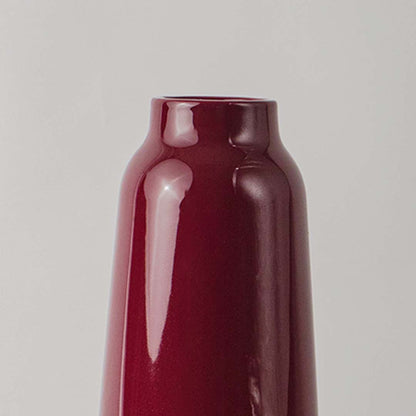 Closeup image of a modern glossy deep red burgundy ceramic vase showing its smooth reflective finish and elegant curved neck.