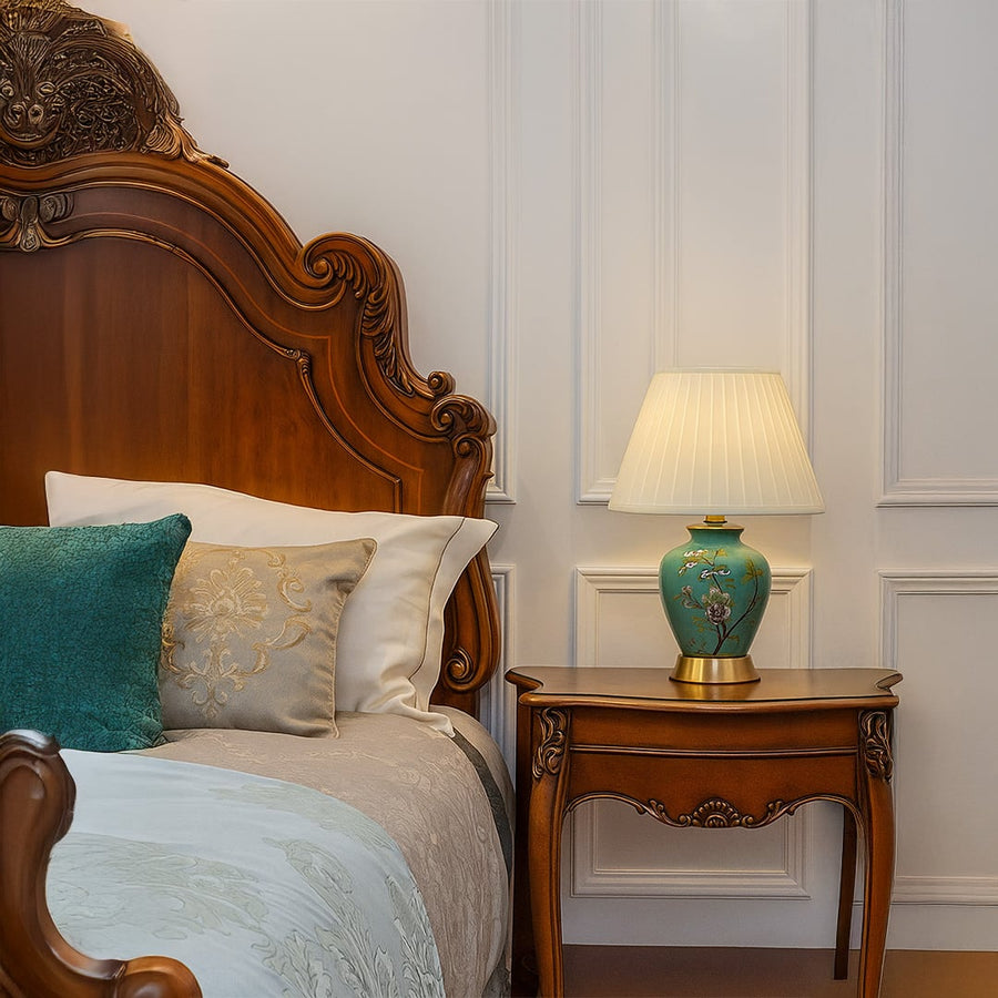 Green ceramic table lamp with floral hand-painted design and pleated fabric shade adding elegance to bedroom decor.