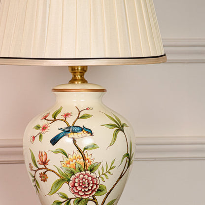 Closeup view of white ceramic table lamp highlighting hand painted floral bird detailing smooth glaze and brass base finish.