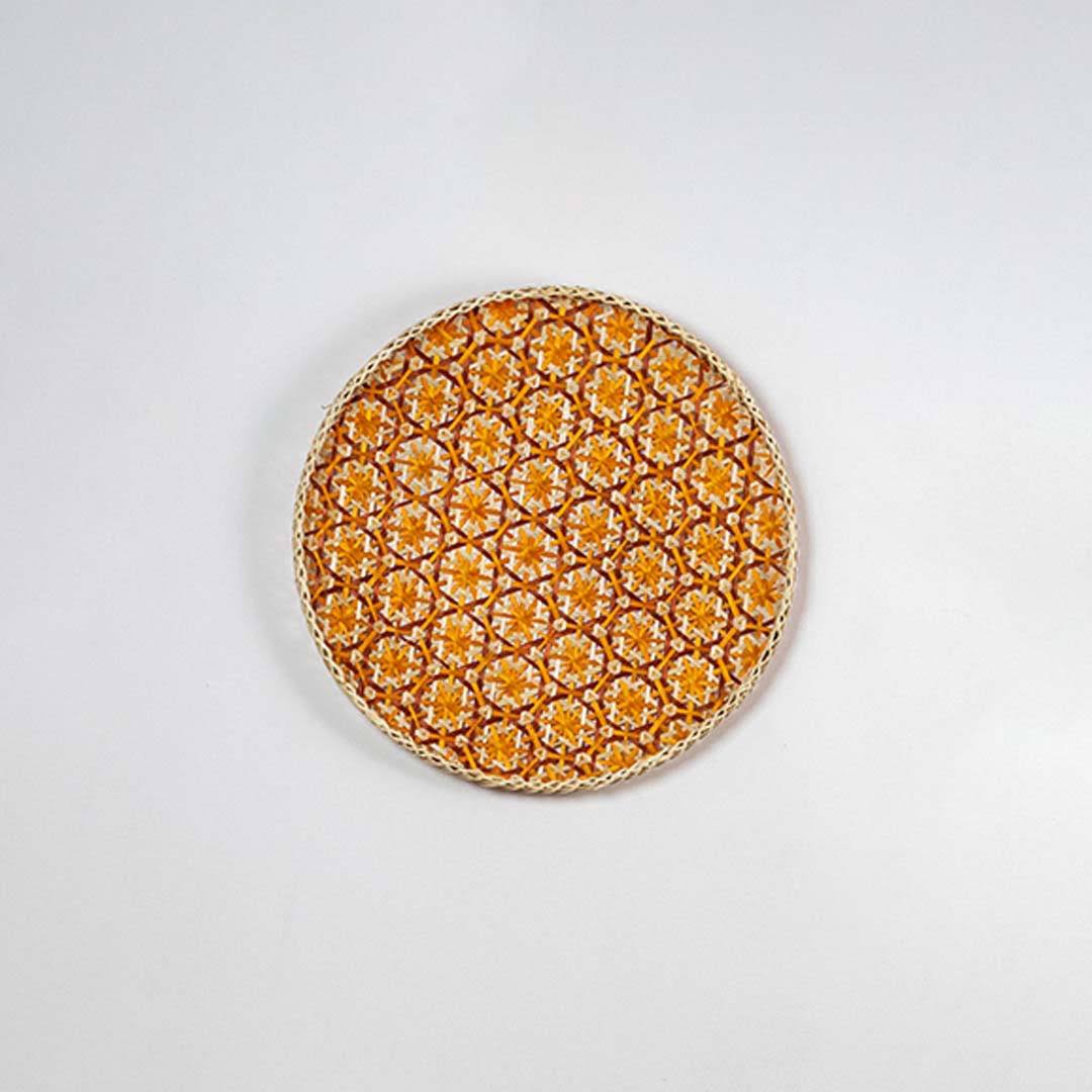 Round handcrafted orange and natural seagrass wall basket with geometric pattern on white background image.