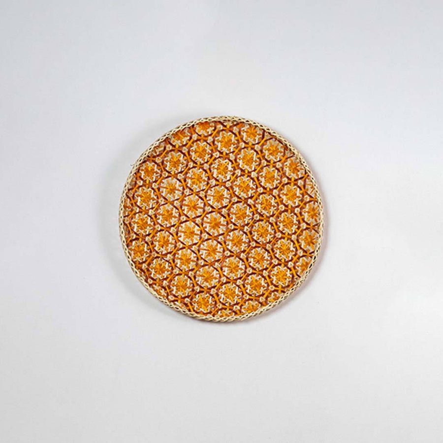 Round handcrafted orange and natural seagrass wall basket with geometric pattern on white background image.