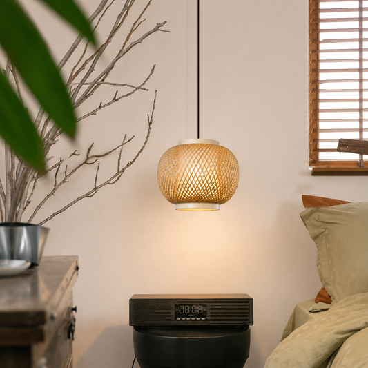 A woven rattan pendant lamp glowing with warm light, hanging in a cozy bedroom setting next to a bed and a digital side table.