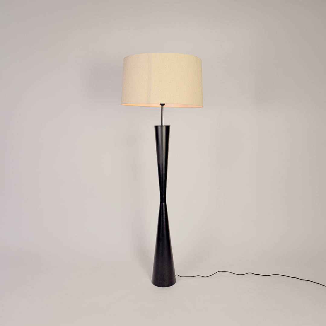 Modern floor lamp glowing on clean white background showing tall black stem wide fabric shade and stable round base with soft warm illumination.