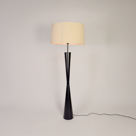 Modern floor lamp glowing on clean white background showing tall black stem wide fabric shade and stable round base with soft warm illumination.