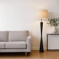 Modern floor lamp styled beside sofa and side table in bright living room creating warm ambient glow with fabric shade and slim black base.