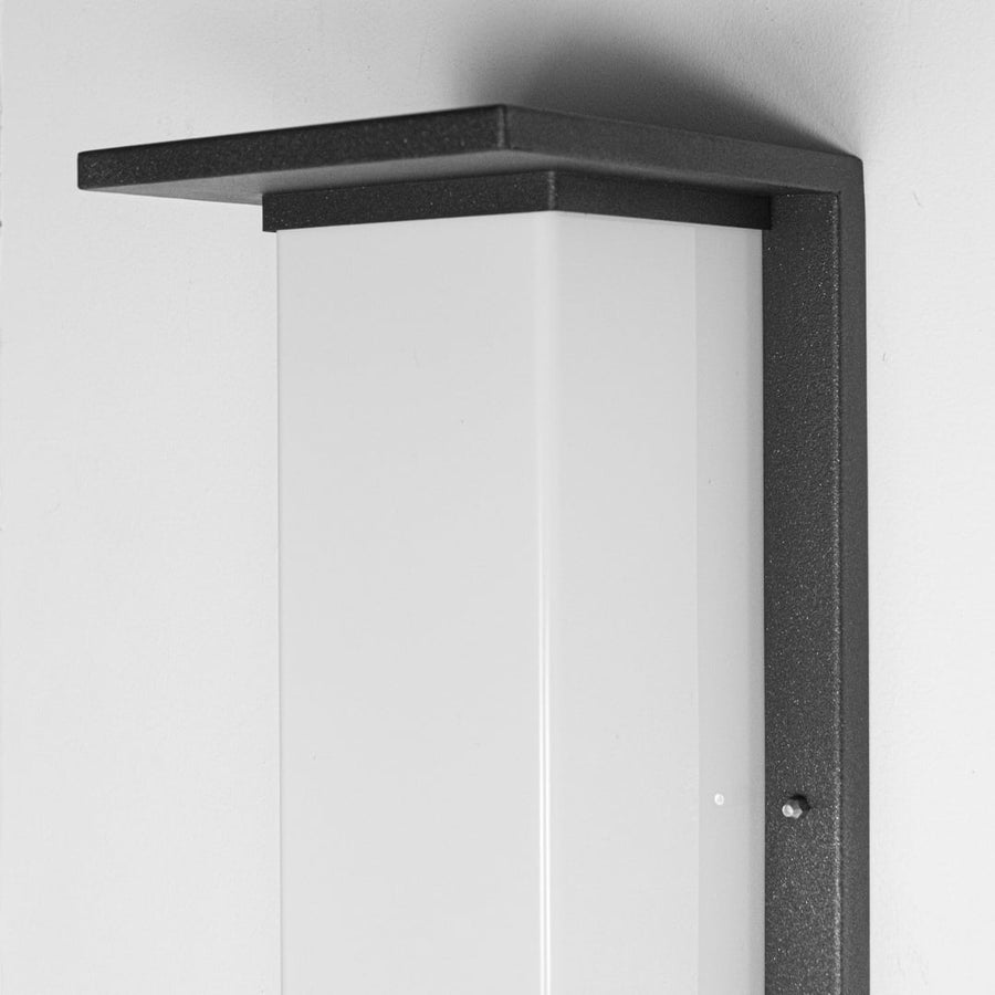 Closeup of modern outdoor wall light showing slim black metal housing frosted diffuser and clean architectural detailing.