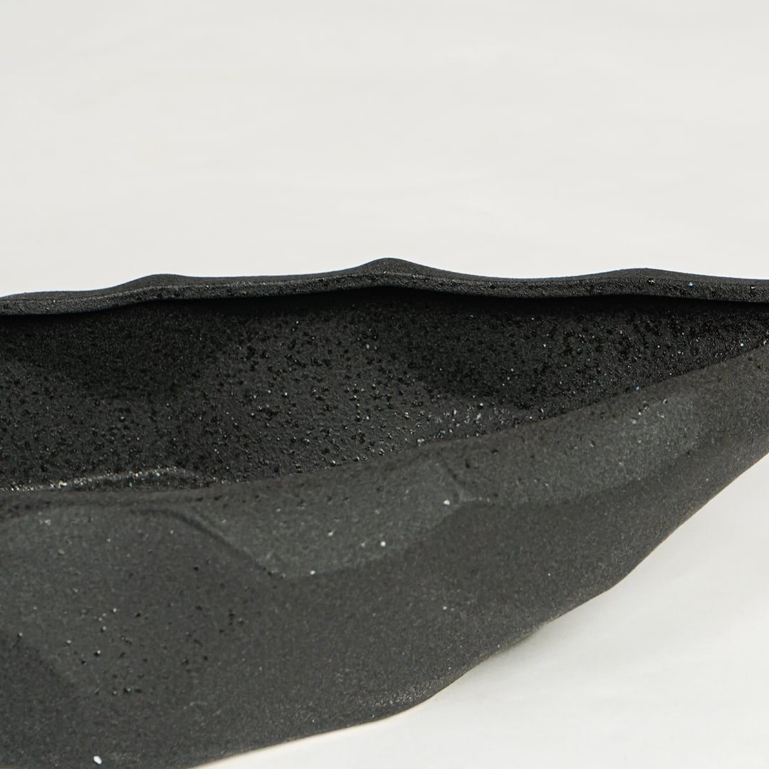 Close view of black ceramic decorative platter highlighting textured matte surface and angular faceted design.
