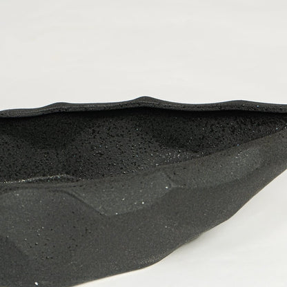 Close view of black ceramic decorative platter highlighting textured matte surface and angular faceted design.