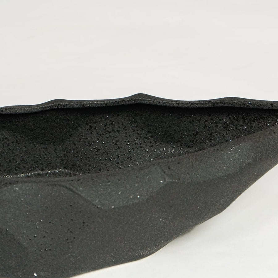 Close view of black ceramic decorative platter highlighting textured matte surface and angular faceted design.