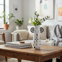 Lifestyle image of an abstract white ceramic vase with black eye loop handles styled with white tulips on a coffee table.
