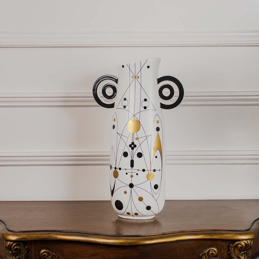 Abstract geometric white ceramic vase with black loop handles displayed on a classic wooden console table for home decor.