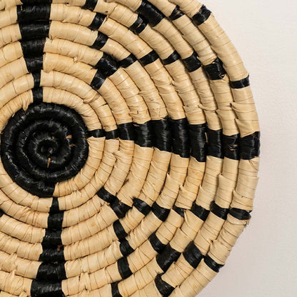 A closeup view of the natural and black rattan wall decor plate showing its detailed starburst weave and textured handcrafted design for warm earthy home styling.
