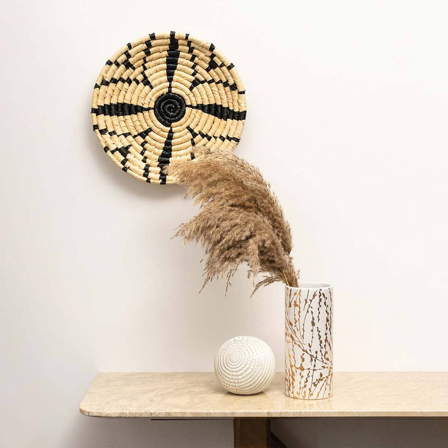 Handcrafted black cream seagrass wall basket with starburst pattern in lifestyle living room setting for boho home decor.