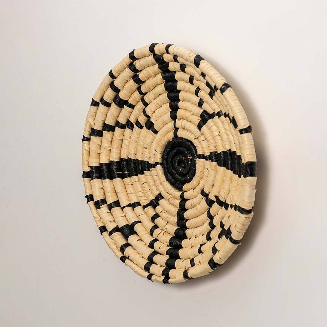 Side view of handcrafted black and cream woven seagrass wall basket with geometric starburst pattern for boho wall decor.
