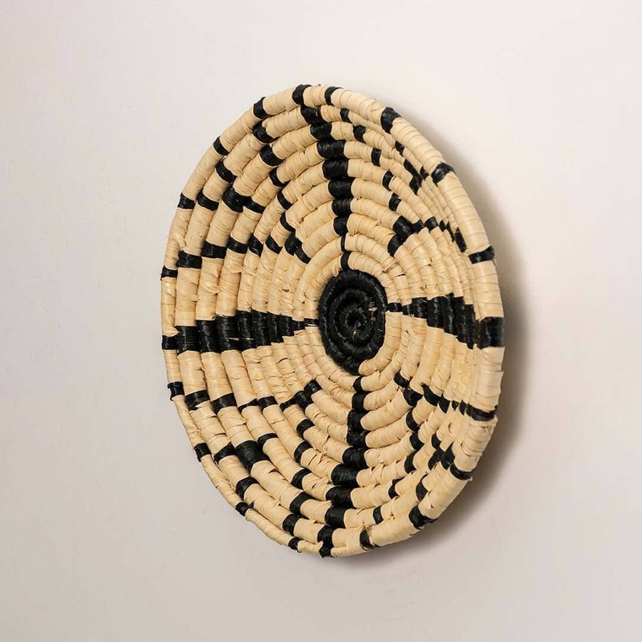 Side view of handcrafted black and cream woven seagrass wall basket with geometric starburst pattern for boho wall decor.