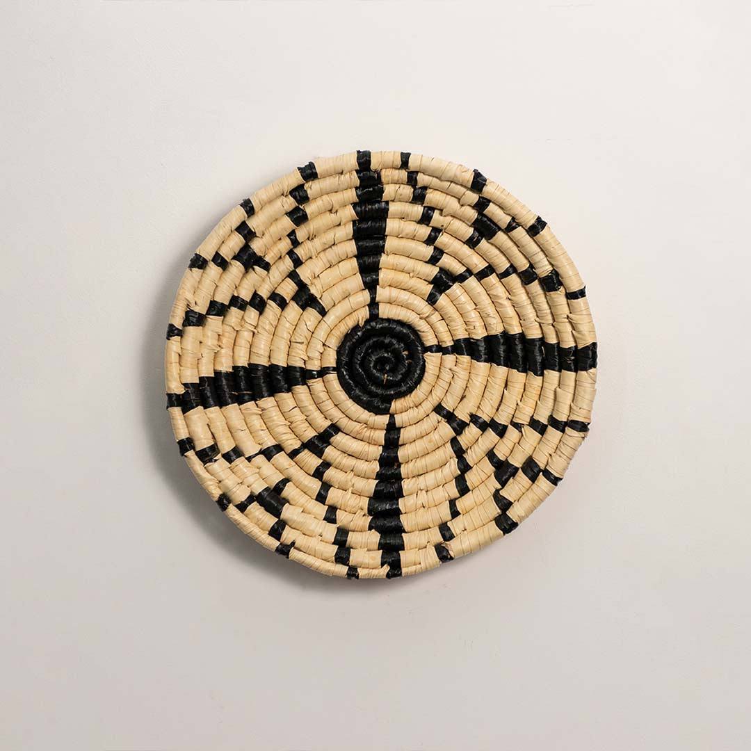 Round handcrafted black and cream woven seagrass wall basket with geometric starburst spoke pattern on white background.