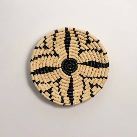 Round handcrafted black and cream woven seagrass wall basket with geometric starburst spoke pattern on white background.