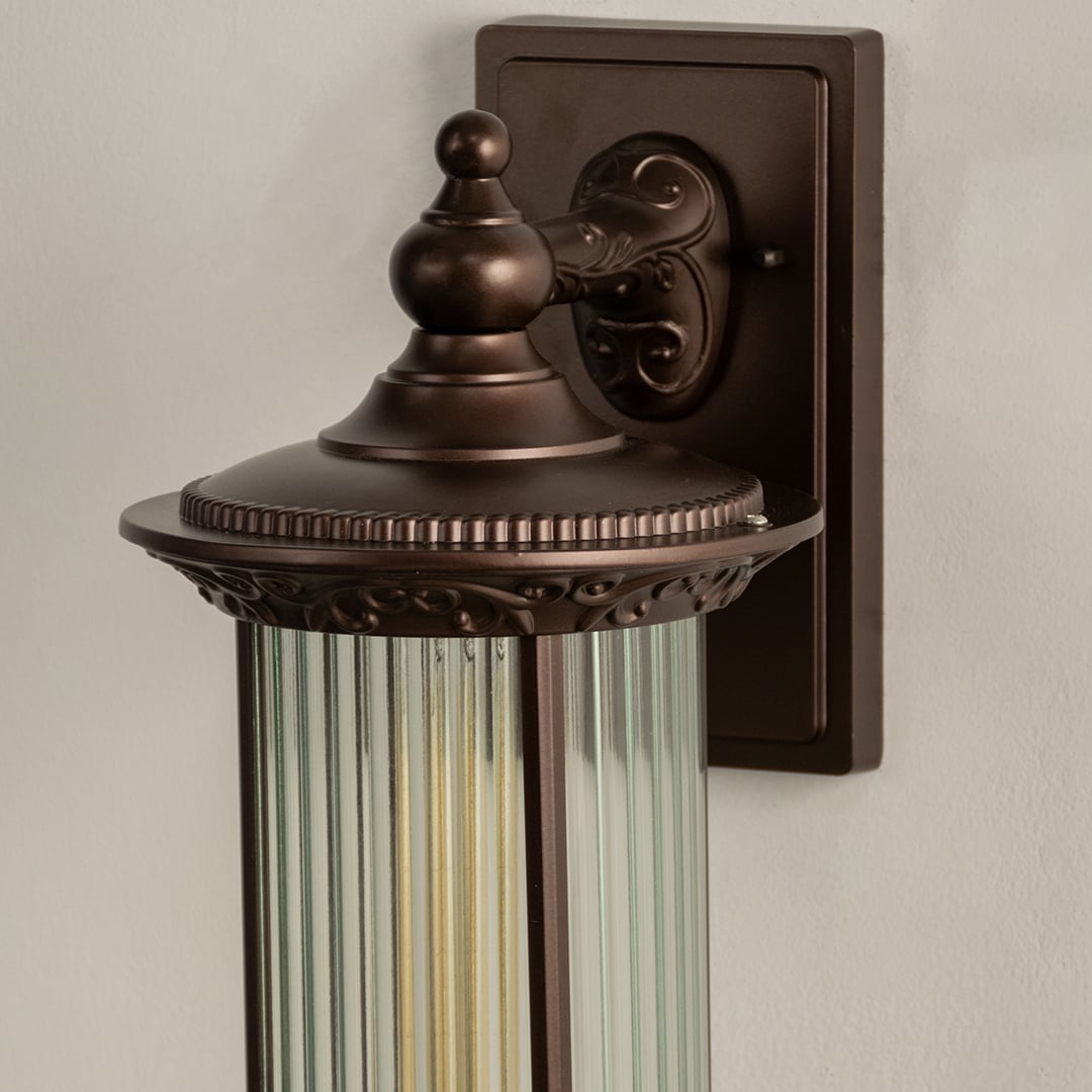 A closeup of the bronze outdoor lantern focusing on the ribbed glass cylinder and ornate bronze detailing that enhances its traditional and decorative appearance.