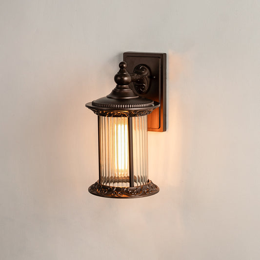 Antique bronze outdoor wall light on white background with cylindrical reeded glass shade for premium entryway decor.