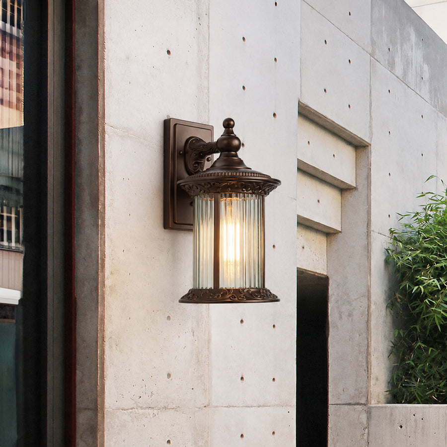 Antique bronze outdoor wall lantern lifestyle image with fluted glass shade mounted on a modern concrete accent wall.