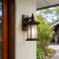 Rustic bronze metal textured glass cylinder wall lantern on exterior stucco facade next to wooden door for porch lighting.