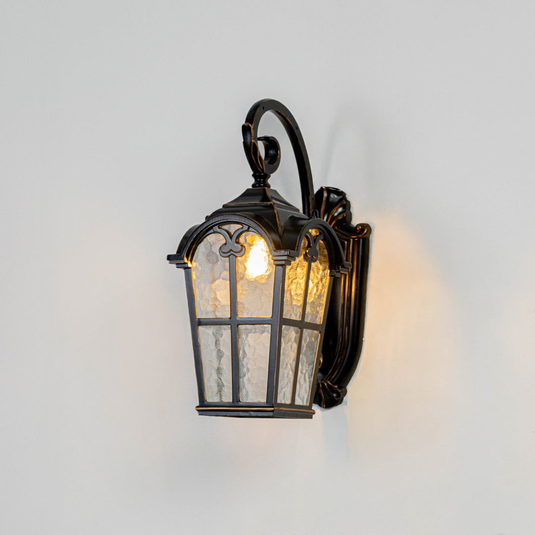 Black metal outdoor wall light on white background with textured seeded glass paneled shade for entry patio decor.