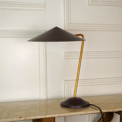 A modern table lamp with a dark brown conical shade and base, and a curved gold metal stem, shown on a marble tabletop against a white paneled wall.