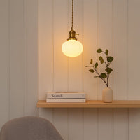 White glass and gold metal pendant light creating warm ambience above dining table in modern interiors.