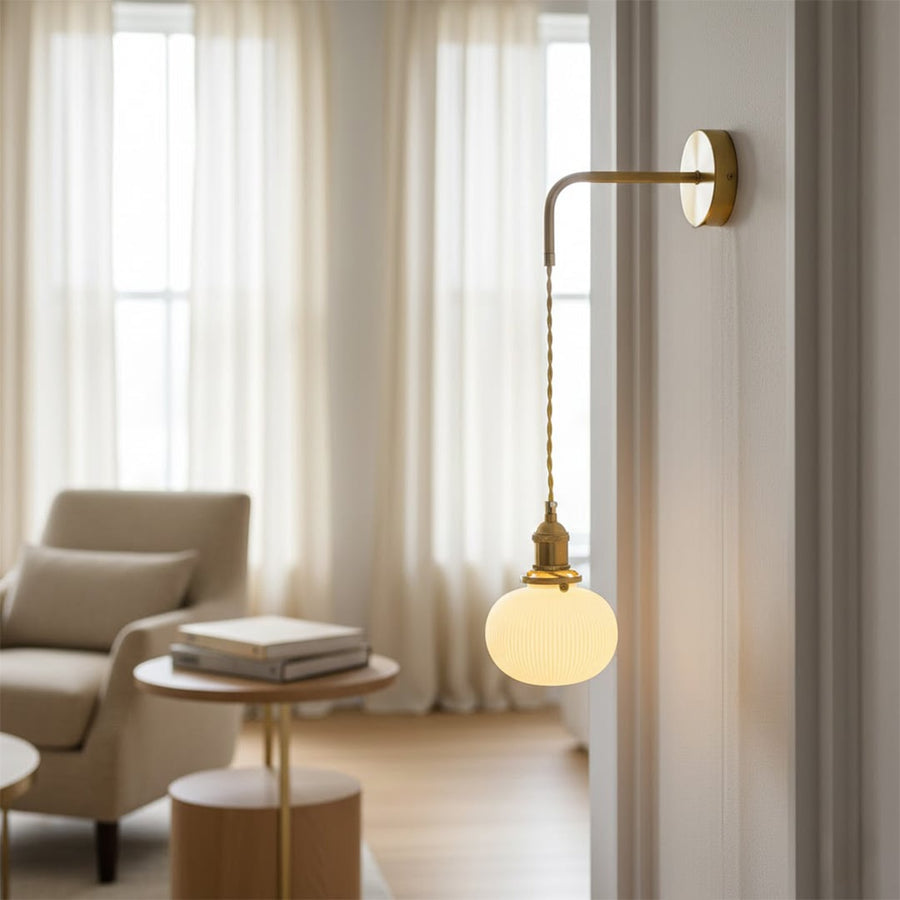 Gold metal hanging wall light lifestyle image with globe glass shade for cozy minimalist interior wall decor.