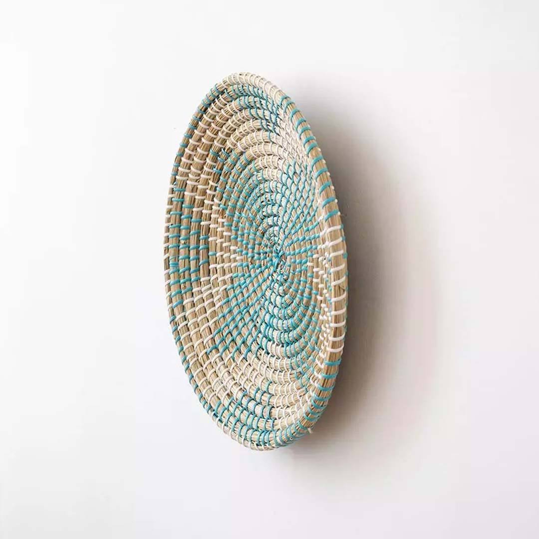 Handwoven seagrass round wall basket decor in natural beige and teal with raised woven profile shown on white background.