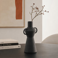 Black textured ceramic flower vase with dried branches placed on table for modern home decor styling.