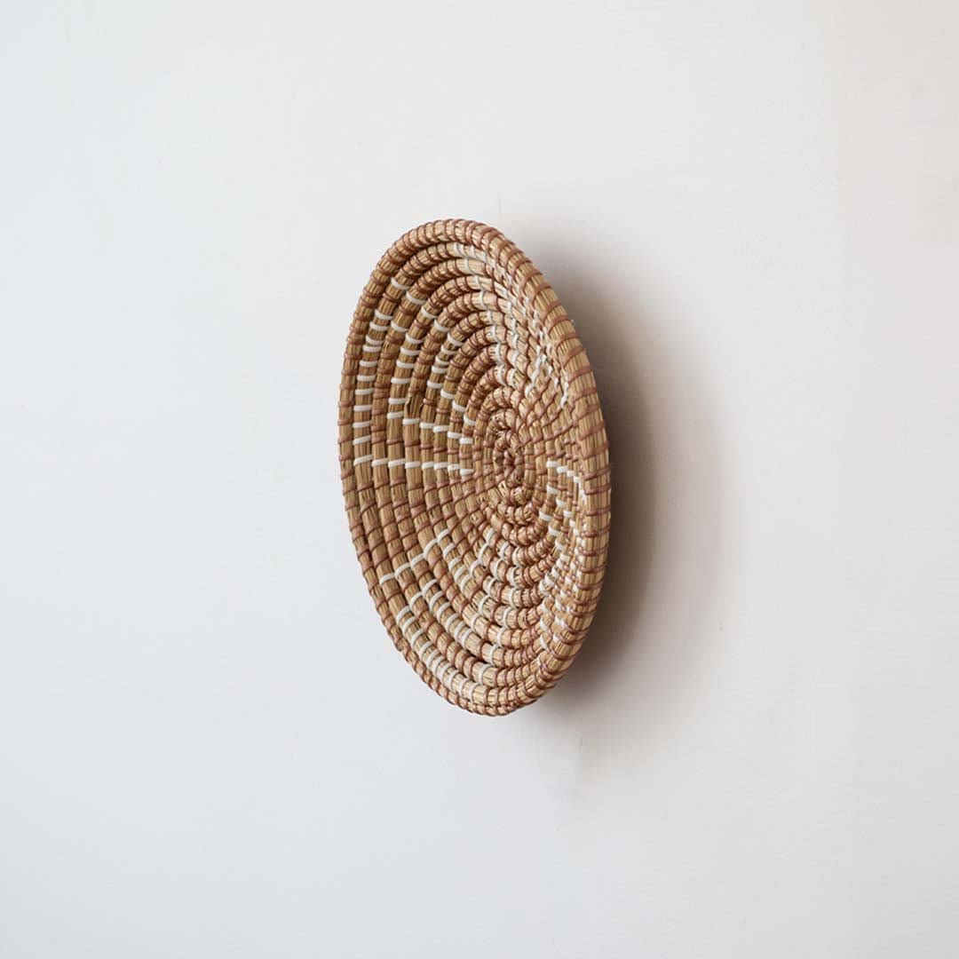 Side angle view of a geometric brown woven seagrass wall hanging basket plate showing depth details on a white wall.